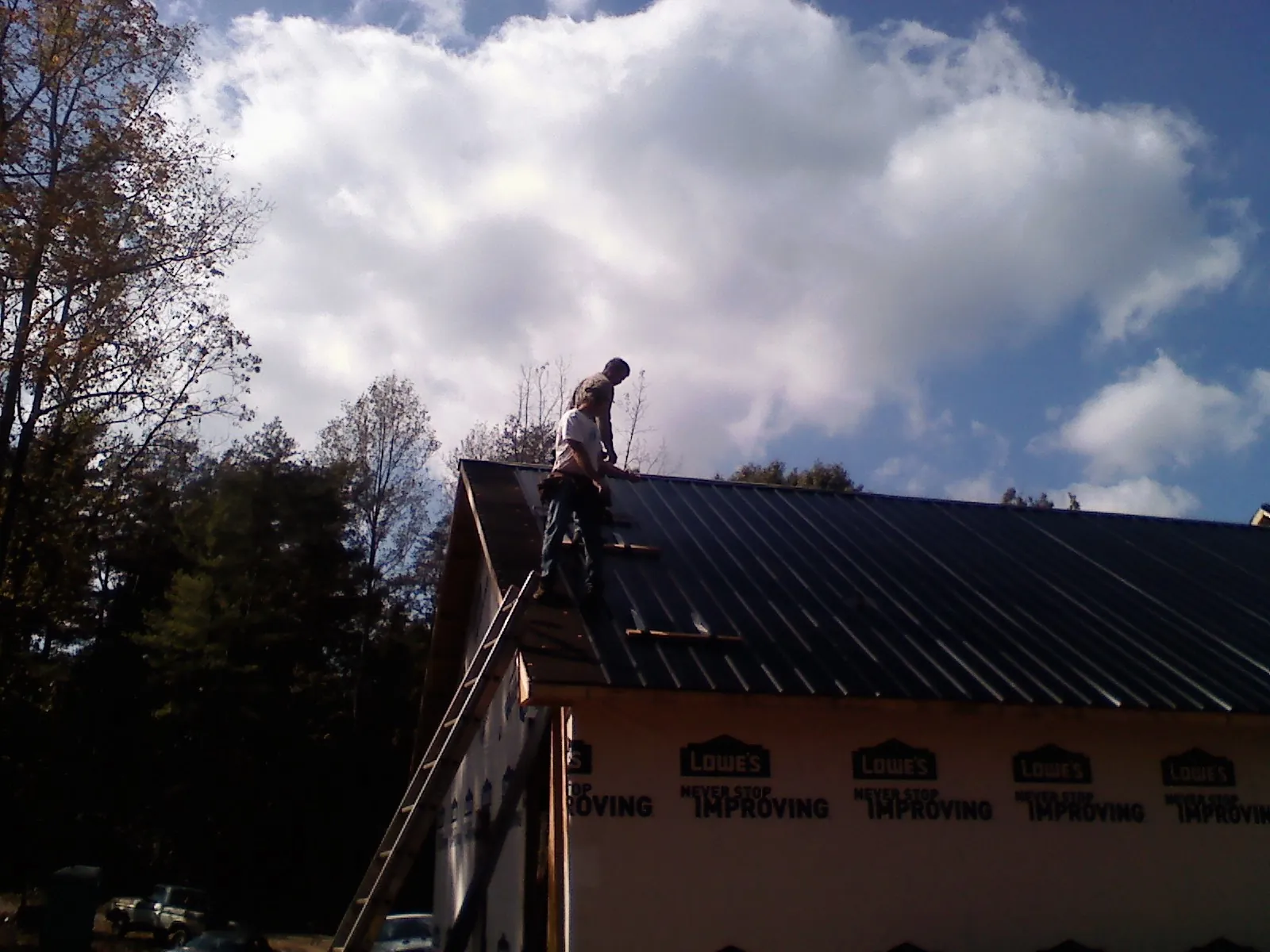 Roofer fastening dark metal panels high against a cloudy sky, from a Roof Inspection job in Addyston