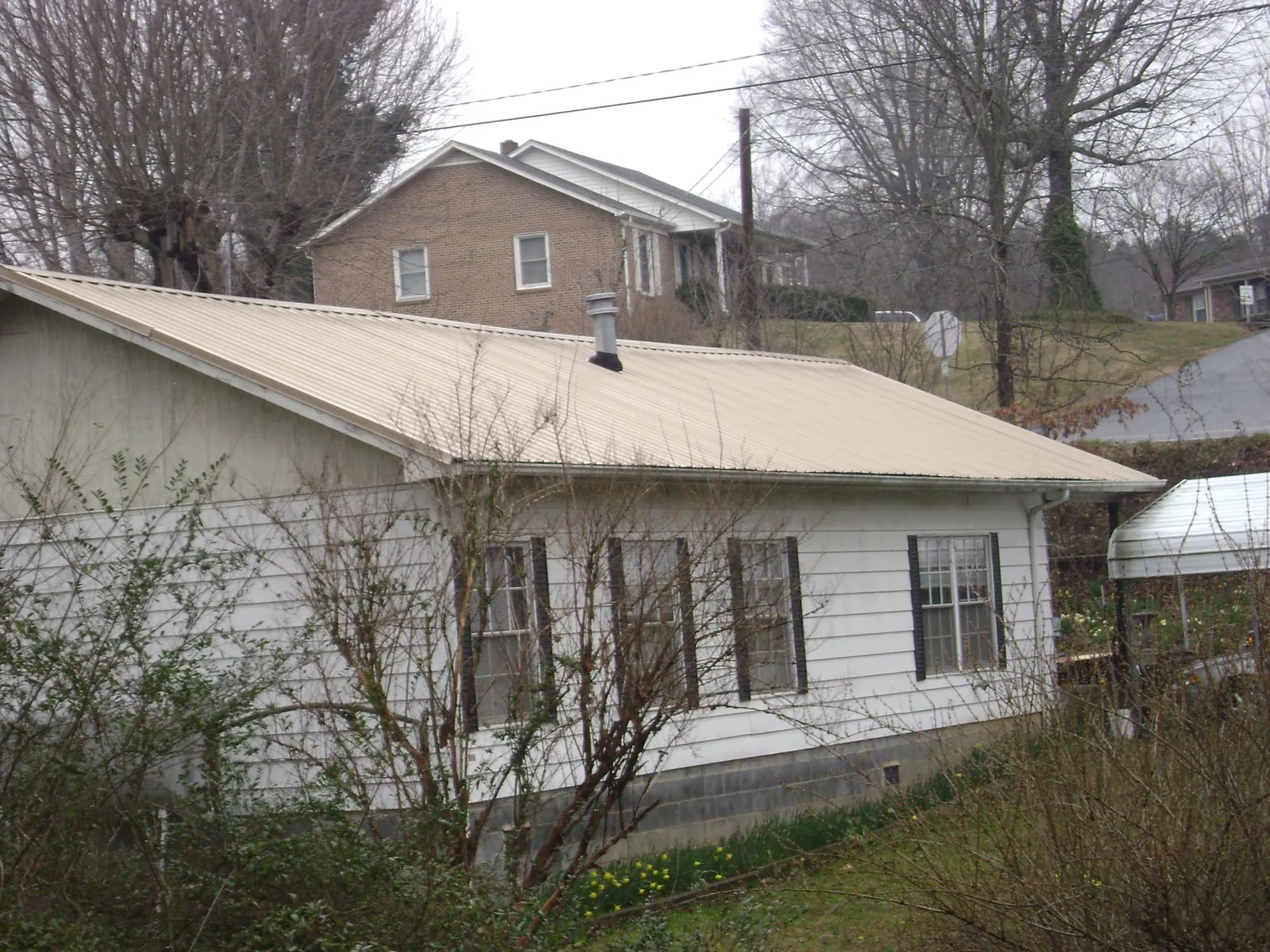 Tan metal roof on a white sided house set into a hillside — Commercial Roofing by Roofing Brothers in Addyston